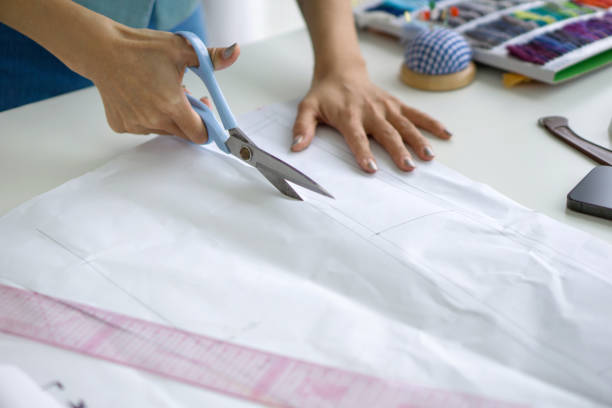 istock Closeup dressmaker hand use scissors to cut sketch paper pattern. 1446005416