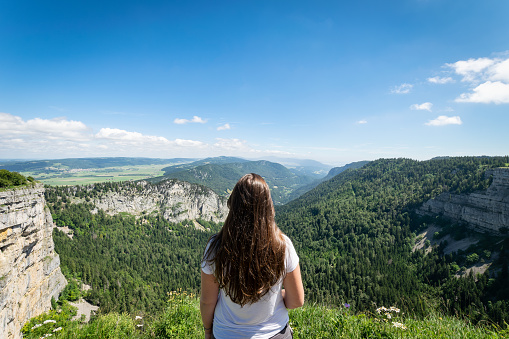 Rear view of a young woman with long hair contemplating the scenery in the Creux-du-Van on a sunny summer day near Le Soliat, Neuchâtel, Switzerland