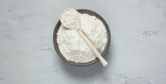 Wheat flour in a plate with a spoon on a gray background.
