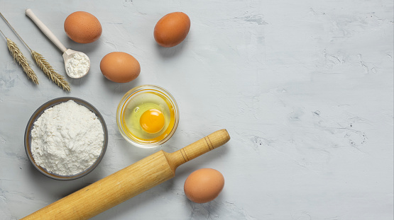 Flour, eggs, rolling pin and wheat spikelets on a gray background with a copy space. Making bread.