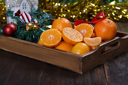 Fresh Clementines or Tangerines in the Basket on Brown Wooden Table with Xmas Lights and Tree Branches