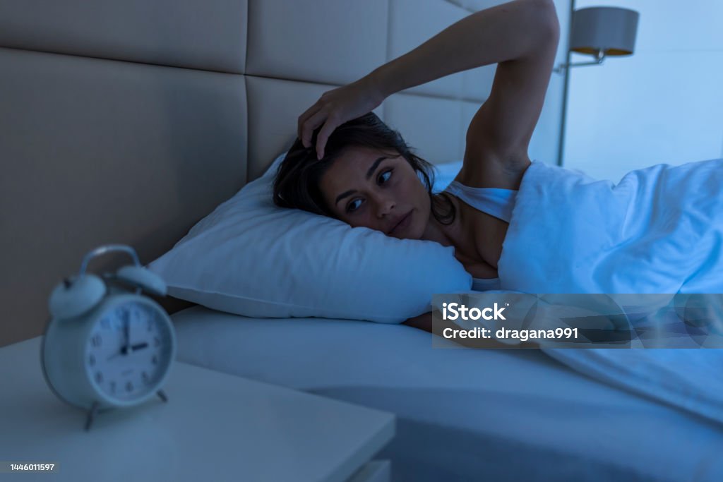 Sleepless woman suffering from insomnia, sleep apnea or stress. Sleepless woman suffering from insomnia, sleep apnea or stress. Tired and exhausted lady. Headache or migraine. Awake in the middle of the night. Frustrated person with problem. Alarm clock. Bed - Furniture Stock Photo