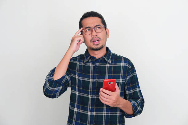 istock Adult Asian man showing thinking pose while holding his handphone 1446012533