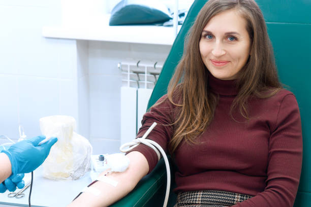 Donor donates blood in medical clinic. Beautiful European woman of 30 years sits in medical chair looking into camera and smiling. Topic of blood donation and saving lives. Donor donates blood in medical clinic. Beautiful European woman of 30 years sits in medical chair looking into camera and smiling. Topic of blood donation and saving lives.. blood plasma stock pictures, royalty-free photos & images