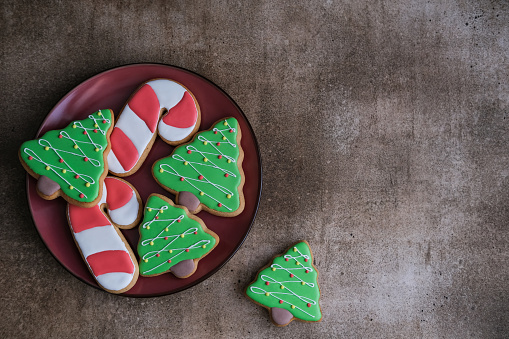 Top view of plate with christmas cookies on brown background with copy space. Christmas tree shaped gingerbread.