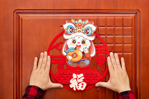 man sticking a Chinese New Year of Rabbit decoration to a door at horizontal composition translation of the Chinese words are lucky and fortune no logo no trademark