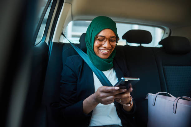 улыбающаяся мусульманская бизнесвумен переписывается по телефону в такси - mobile phone seat belt text messaging smiling стоковые фото и изображения