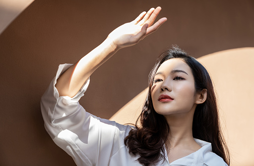 Portrait of young beautiful asian woman traveler hands protect face from sun light in fresh summer time. Happy cheerful asian girl in summer. Beauty sunscreen skin care make up model concept