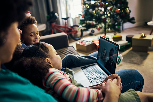 Family, children and laptop in video call for Christmas celebration, meeting or staying connected at home. Happy kids relax with parents on living room sofa on computer talking online to grandparents