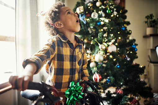 Boy, child and surprised with christmas bike in relax family home and house living room in festive holiday, gift opening and celebration. Kid, wow face and shocked and xmas bicycle present in lounge