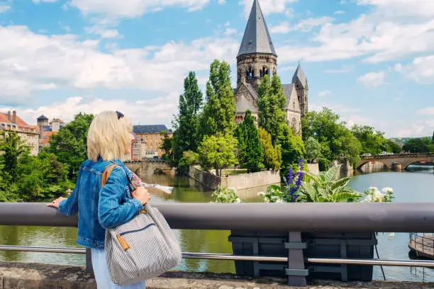 Woman viewing the Romanesque Protestant church, the Temple Neuf, by the Moselle River from Pont Moyen in the town of Metz in the north east of France.