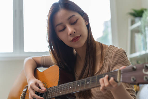 istock Young  woman sitting on the sofa and playing guitar. 1446031317
