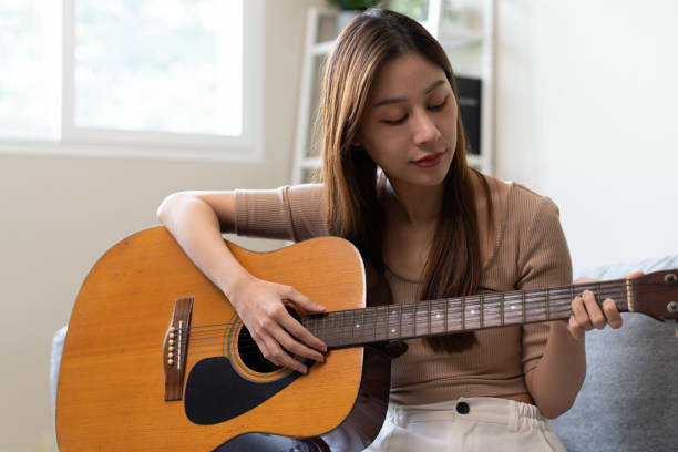 istock Young  woman sitting on the sofa and playing guitar. 1446031348