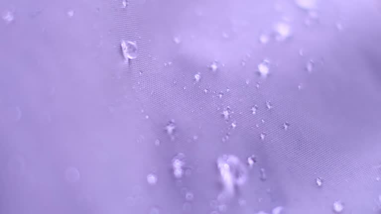 Slow Motion Shot of Water Splashing on waterproof fabric. water beading on fabric. Waterproof coating background with water drops. soft focus, blur