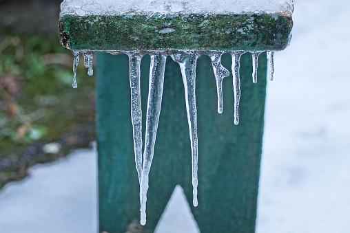 a row of icicles on a green wooden bench board in white snow on a winter street