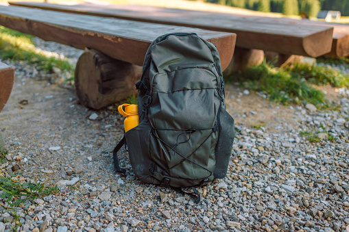 Travel backpack on the wooden bench in the forest. Outdoor wanderlust items. Travel, tourism and camping equipment. Picnic rest on the nature. Summer active hiking and trekking tools.