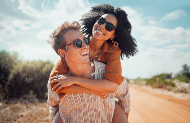 Love, happy and couple piggy back on road path in Arizona desert in USA for romantic getaway. Interracial people dating smile while enjoying summer romance on travel holiday adventure together. amor, feliz y pareja de vuelta en el camino de la carretera en el desierto de arizona en ee.uu. para una escapada romántica. las personas interraciales que salen sonríen mientras disfrutan del romance de verano en la aventura de vacaciones de viaje junto