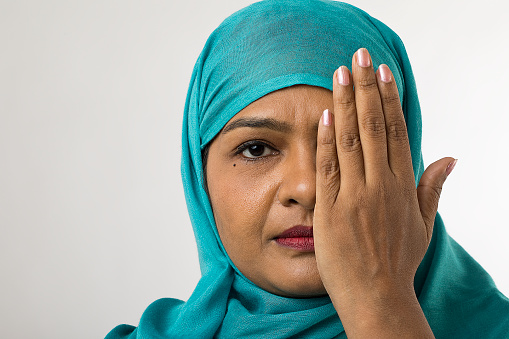 Portrait of mid adult woman wearing blue hijab and coving her face against white background