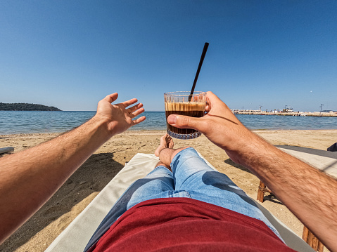 Young man drinking freddo cappuccino on the beach in Thasos, Greece. His POV.