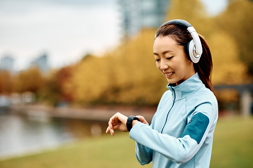 Happy Asian sportswoman using smart watch while working out in the park.
