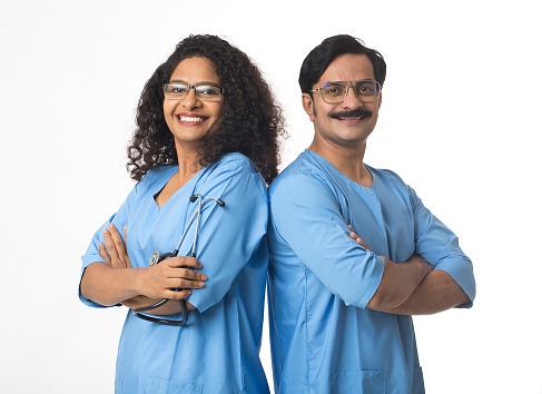 Portrait of smiling male and female surgeons wearing medical scrubs with arms crossed standing together against white background