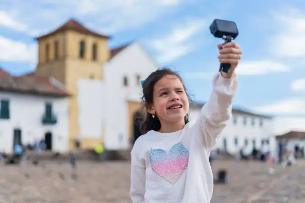 Latina girl with an average age of 7 years dressed comfortably is in the historic square of Villa de Leyva boyaca to which she traveled with her family taking a selfie with her gopro