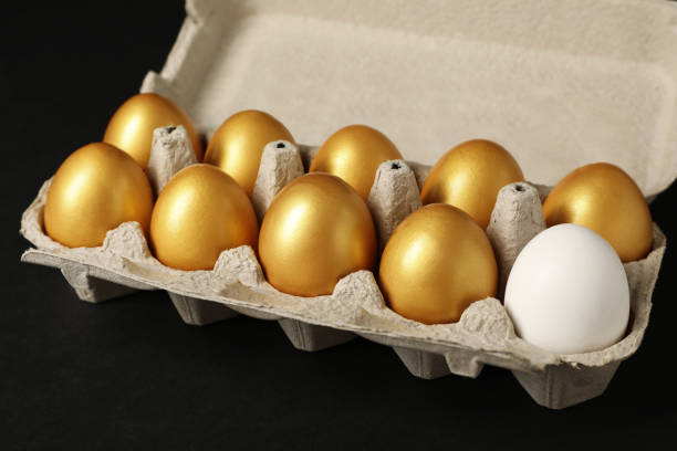 huevo de gallina ordinario entre los dorados en caja sobre fondo negro, primer plano - carton multi colored easter egg easter fotografías e imágenes de stock