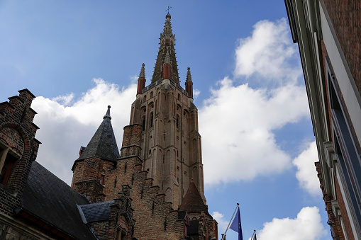 Bruges, Belgium - September 11, 2022: A 115-meter brick tower that is part of the medieval Church of Our Lady against the backdrop of the summer sky