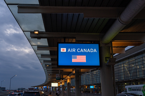 Mississauga, Ontario, Canada - July 5, 2022: Air Canada sign at passenger drop-offs curbside in Toronto Pearson International airport in early morning, Mississauga, Ontario, Canada.