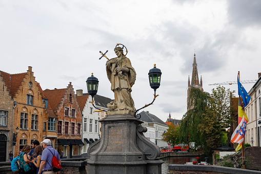 Bruges, Belgium - September 7, 2022: The statue of John of Nepomuk is an outdoor sculpture, installed on the side of the bridge over the canal in the old town of this medieval city