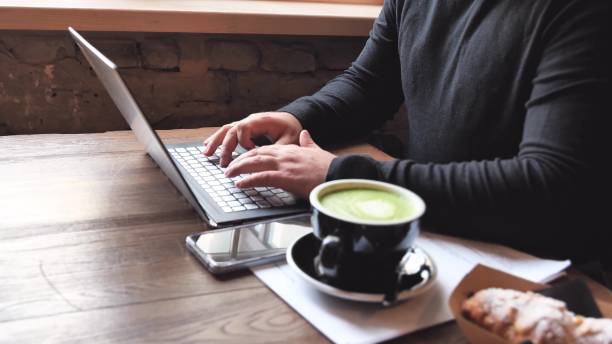 Male freelancer working with laptop computer, businessman work, typing on notebook while sitting at wooden table in modern coffee cafe with cup of coffee. Modern business, distance job, selfemployer. Selective focus