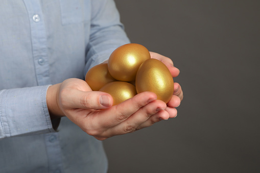 Woman holding shiny golden eggs on grey background, closeup