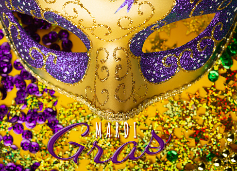 Mardi Gras gold color beads with Luxury Masquerade venitian festival carnival mask and golden, green, purple confetti on yellow background. Party invitation, greeting card, venetian carnivale celebration concept.