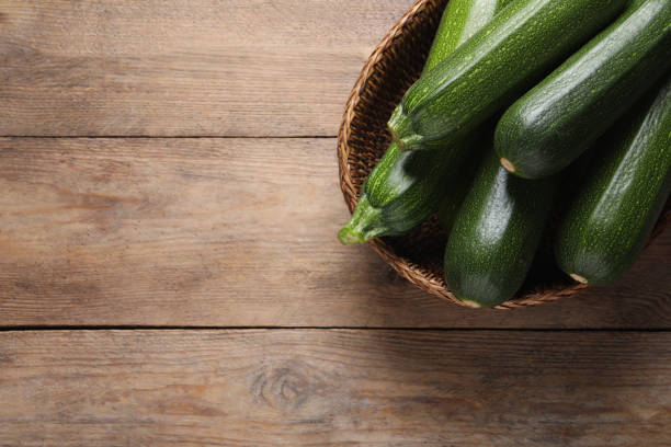 istock Raw ripe zucchinis in wicker basket on wooden table, top view. Space for text 1446050095