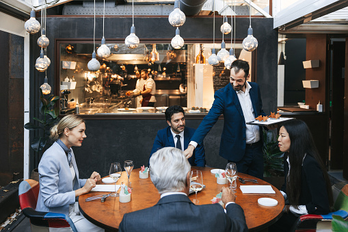 Group of business people dining in a restaurant while the waiter is serving their appetizers.