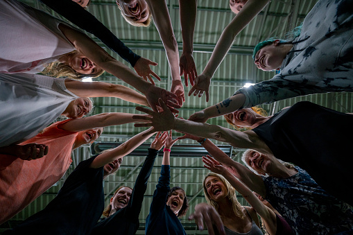 A low-angle, wide shot of a group of women wearing sports clothing in a sports hall in Newcastle Upon Tyne. They huddle together in a circle and put their hands in the middle.