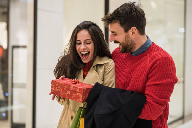 Handsome young man surprising his girlfriend with a Christmas gift stock photo