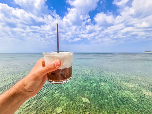 Young man drinking freddo cappuccino on the beach in Thasos, Greece. Holding the cup.