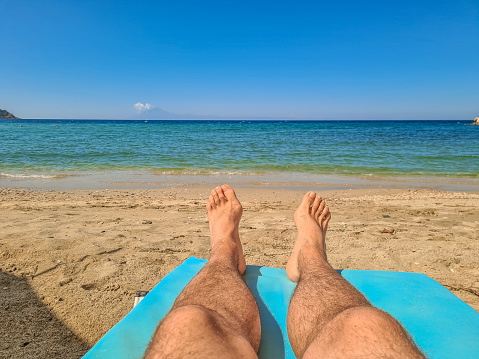 Holiday concept. Woman feet close-up relaxing on beach, enjoying sun and splendid view