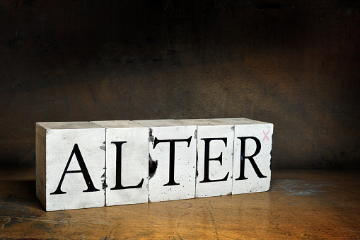 ALTER, word with serifs on old and dirty blocks on old wood in dark surroundings. Different words in the same style can be found below: