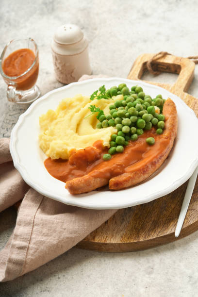 bangers und brei. grillwürste mit kartoffelpüree und grünen erbsen auf weißem teller auf grauem grund. traditionelles gericht aus großbritannien und irland. bbq rindfleischwürste. draufsicht. - mashed potato food staple vertical color image stock-fotos und bilder