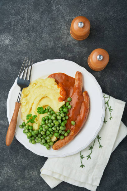 bangers und brei. gegrillte würstchen mit kartoffelpüree und grünen erbsen auf weißem teller auf schwarzem dunklem hintergrund. traditionelles gericht aus großbritannien und irland. bbq rindfleischwürste. draufsicht. - mashed potato food staple vertical color image stock-fotos und bilder