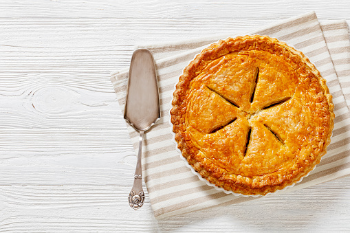 Ground Beef Meat Pie with a flaky puff pastry double crust with hearty minced beef cooked with vegetables and seasoning in white baking dish on wood table, flat lay, free space