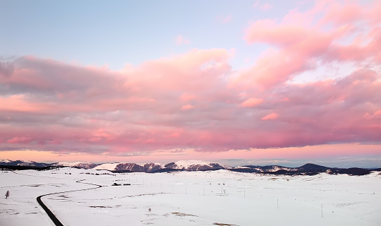 Picturesque drone view of the sunset over a snow covered mountain valley. Winter landscape from a bird's-eye view. Amazing pink clouds on the background of blu sky.
