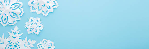 istock White snowflake shapes created from paper on light blue table background. Pastel color. Closeup. Top down view. Wide banner. Handmade decoration elements for winter festive. Empty place for text. 1446064751