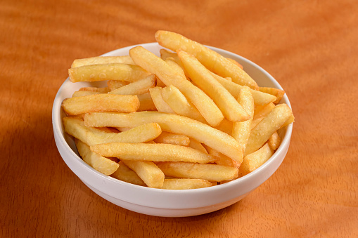 French fries. Small portion of chips in white bowl on wooden background.