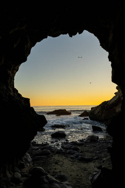 Two Planes Flying by, Viewed from a Cave Leo Carrillo State Beach and its rocky shoreline and large coastal caves, taken during sunset. Two t-6 Texan, single engine plane, flying by while seen from inside a cave. rock sea malibu silhouette stock pictures, royalty-free photos & images