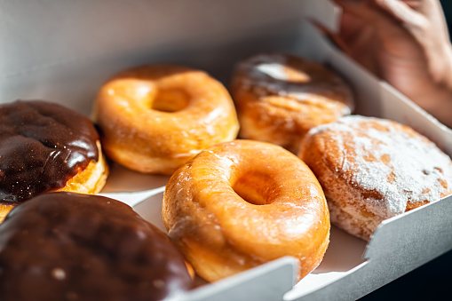 Man holding half a dozen of donuts doughnuts in carboard container box, glazed deep fried dessert pastry of Boston cream, chocolate filling