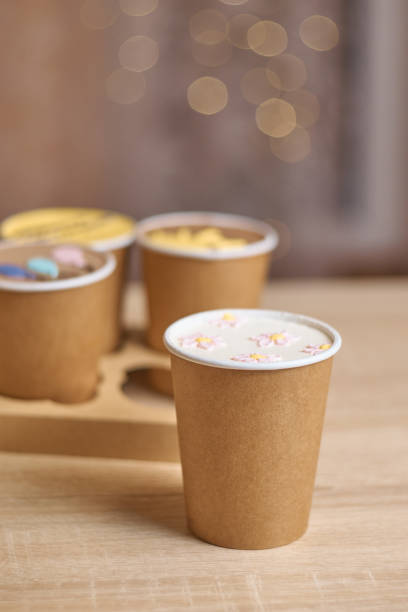 four homemade mini chocolate cake to go in coffee cup on a table, confectionery concept. fashionable dessert. paper cups with cakey are in a box. Vertical, copy space, bokeh background, soft selective focus un vaso de papel con pastel para acompañar con crema dibujando flores sobre una mesa y tres mini tartas de chocolate caseras en tazas de café en una caja sobre el fondo, concepto de tendencia de confitería. vertical, espacio de copia, bokeh