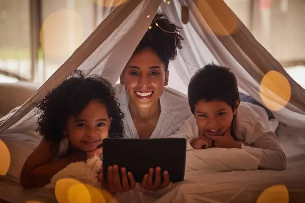 Photo of Family portrait, tablet and online app for kids cartoons, streaming and digital night story in blanket fort tent at home. Happy Brazil mother, smile children and reading, playing on internet tech